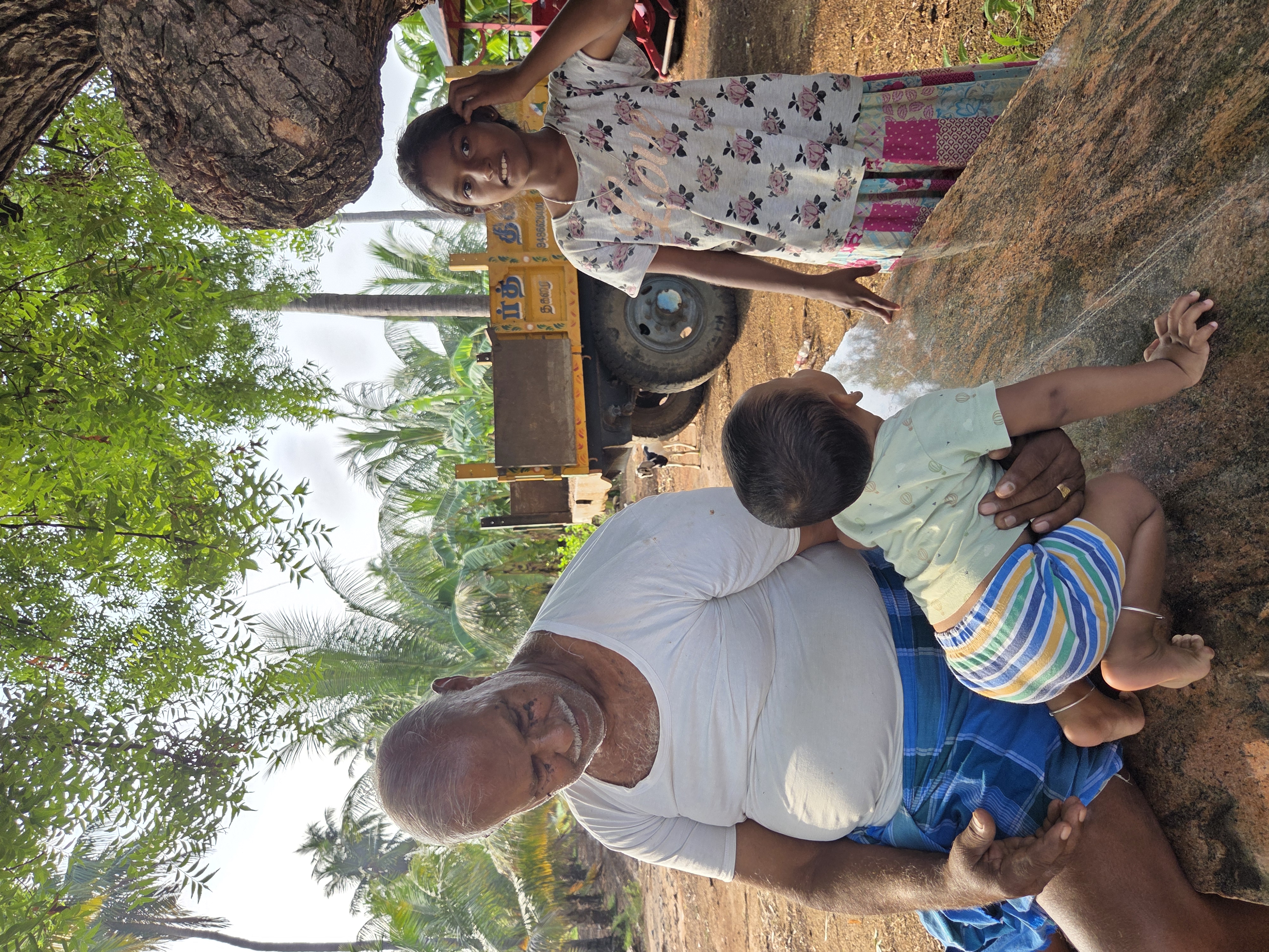 Mr. Sengottaian with his grandchildren beside the tractor, a goat grazing behind